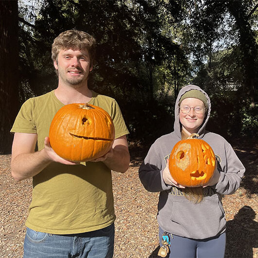 Two people smiling and holding their carved pumpkins